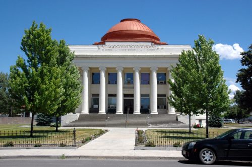 Historic courthouse with a domed roof, flanked by trees and a clear blue sky.