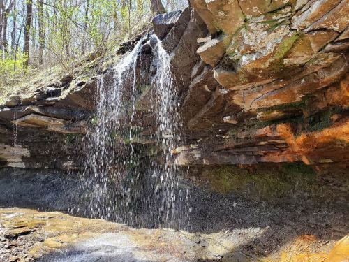 A small waterfall cascades over rocky cliffs in a lush, green forest setting.