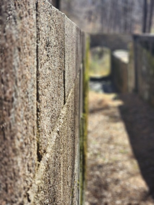Close-up of a textured stone wall with a blurred pathway leading to an archway in the background.