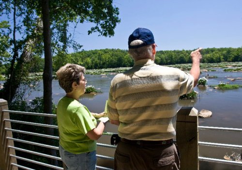 A man and woman stand by a river, pointing and looking at the scenery on a sunny day.