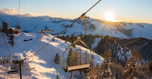 A scenic view from a ski lift at sunset, overlooking snow-covered mountains and trees.