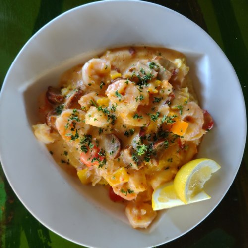 A bowl of shrimp and sausage over creamy grits, garnished with herbs and a lemon wedge.