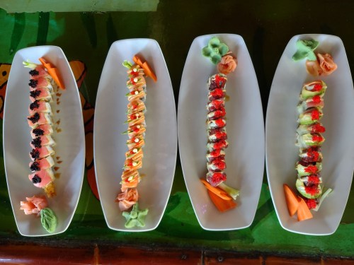 Four elegant sushi platters featuring colorful rolls, garnishes, and wasabi on a vibrant background.