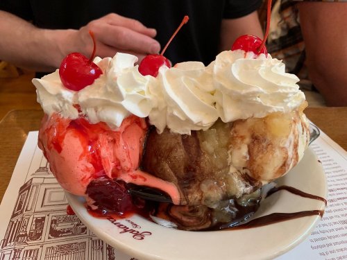 A colorful ice cream sundae with scoops of pink and brown ice cream, topped with whipped cream and cherries.
