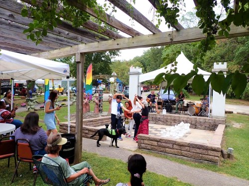 A lively outdoor event with people dancing, a dog, and a band performing under a pergola surrounded by tents.