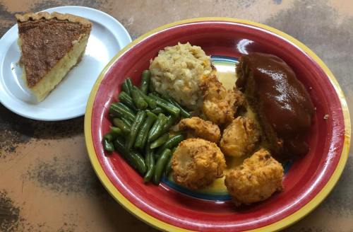 A colorful plate with green beans, rice, meatloaf with sauce, and fried dumplings, alongside a slice of pie.