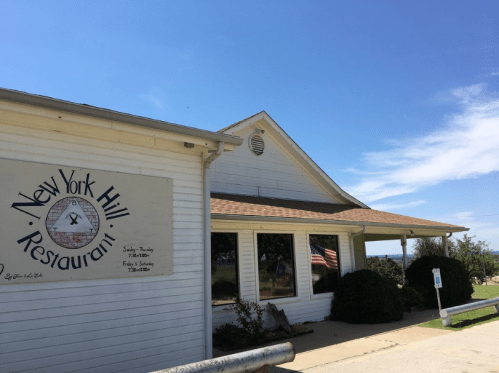 Exterior of New York Hill Restaurant with a sign, American flag, and clear blue sky in the background.
