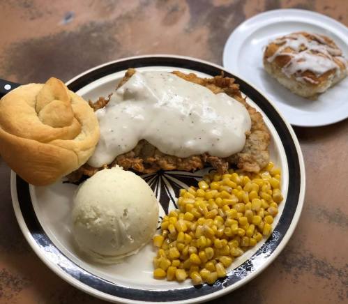 A plate of fried chicken with gravy, mashed potatoes, corn, a roll, and a cinnamon roll on the side.