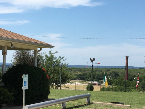A scenic view featuring a building, a weather vane, and distant hills under a clear blue sky.