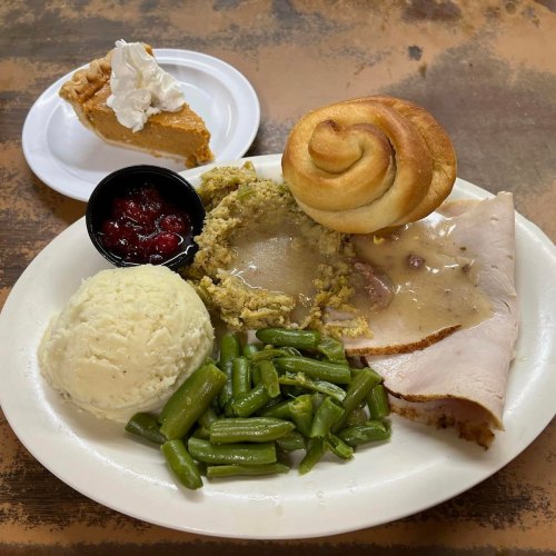 A plate of turkey with gravy, stuffing, green beans, mashed potatoes, a roll, and a slice of pumpkin pie with whipped cream.