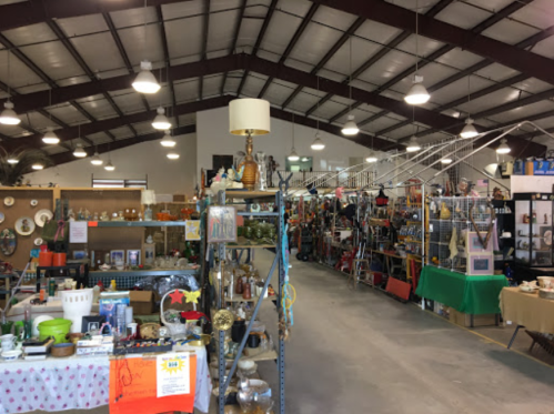A spacious indoor market filled with various antiques and collectibles displayed on shelves and tables.