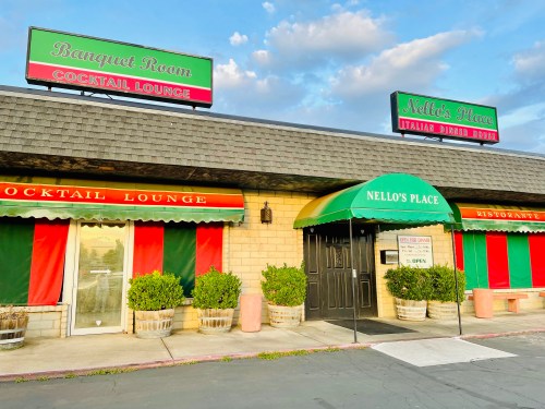 Exterior of Nello's Place, featuring a green awning, red and green curtains, and a sign for the cocktail lounge.