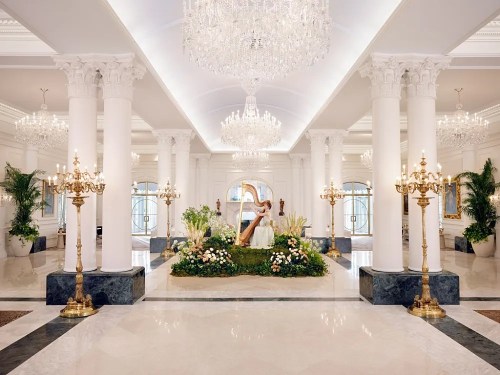 Luxurious hotel lobby with tall white columns, chandeliers, and floral arrangements, creating an elegant atmosphere.