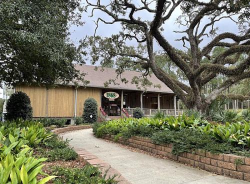 A rustic building with a sign reading "1868," surrounded by lush greenery and a large tree.