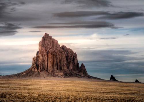A dramatic rock formation rises from a vast, barren landscape under a cloudy sky.
