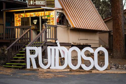 A large white sign spelling "RUIDOSO" in front of a food establishment with a colorful menu display.