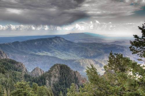 A panoramic view of mountains and valleys under a cloudy sky, showcasing lush greenery and distant peaks.