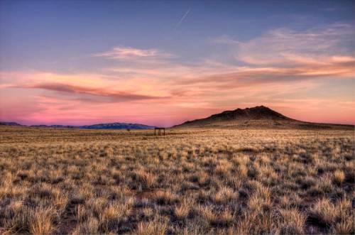 A serene landscape featuring a grassy field, distant mountains, and a colorful sunset sky.