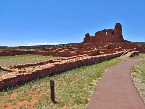 Ancient stone ruins with a pathway, set against a clear blue sky and grassy landscape.