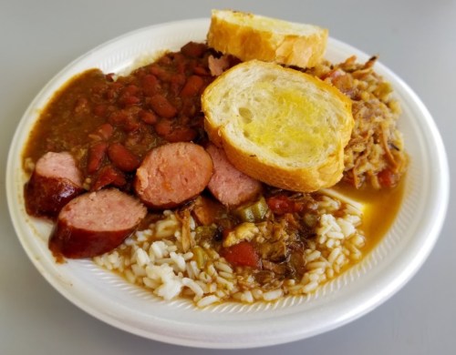 A plate of food featuring sausage, rice, beans, and slices of bread.