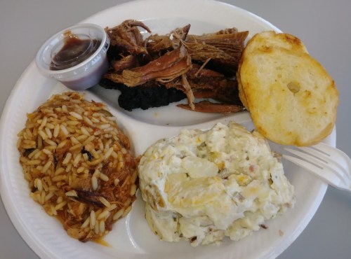 A plate with pulled pork, barbecue sauce, rice, potato salad, and a biscuit.
