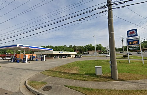 A gas station with a Marathon sign, fuel pumps, and a convenience store, set in a suburban area with green trees.