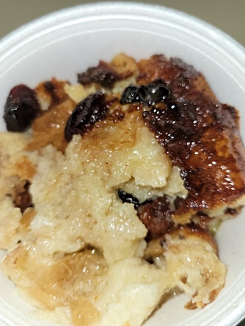 A close-up of a baked dessert with a golden-brown top and dark raisins, served in a white bowl.
