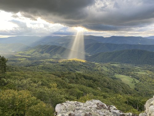 A scenic mountain landscape with sunlight breaking through clouds, illuminating a valley below.