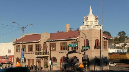 Historic building with a clock tower, featuring a red roof and arched windows, located at a street intersection.