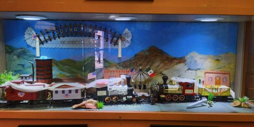 A display case featuring a miniature train set with buildings, mountains, and decorative elements.