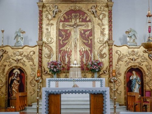 Ornate church altar with a golden crucifix, floral arrangements, and statues of saints on either side.