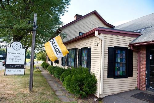 A charming tavern with a sign reading "OPEN" and a landscaped entrance, surrounded by greenery.