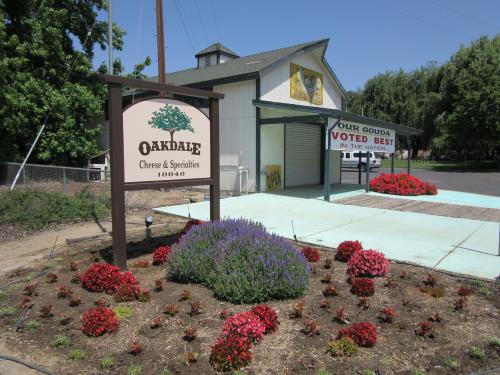 Sign for Oakdale Cheese & Specialties in front of a building, surrounded by colorful flower beds.
