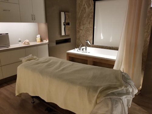 A serene spa room featuring a massage table, a bathtub, and soft lighting, creating a relaxing atmosphere.