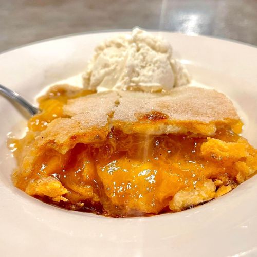 A bowl of warm peach cobbler topped with a scoop of vanilla ice cream.