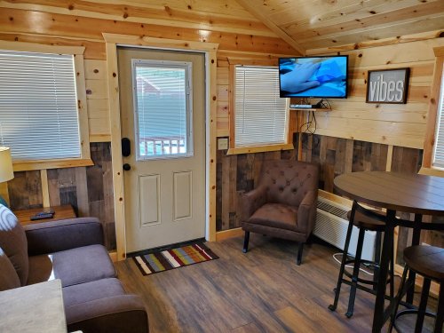 Cozy interior of a cabin with wooden walls, a door, a TV, a chair, and a small dining table.