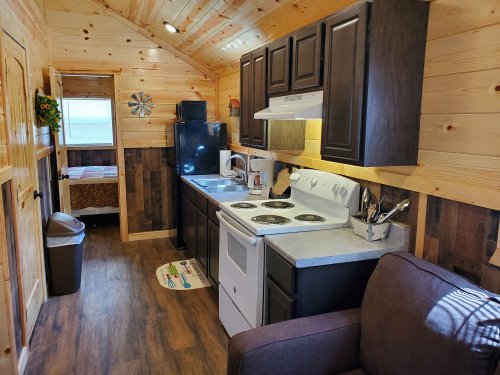Cozy interior of a tiny cabin featuring a kitchen, living area, and wooden walls, with a bed visible in the background.