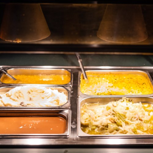 A buffet display with various trays of food, including sauces and dishes, under warm lighting.
