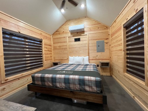 Cozy cabin interior featuring a bed with plaid bedding, wooden walls, and modern amenities.