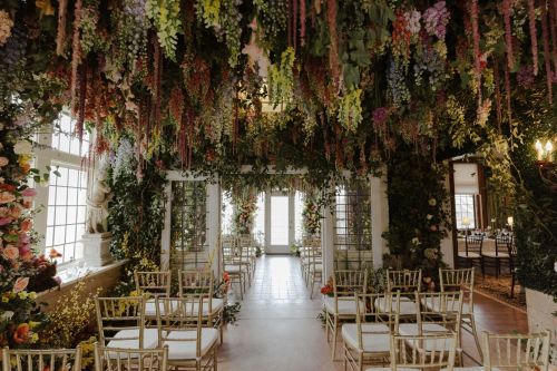 A beautifully decorated indoor venue with lush floral arrangements hanging from the ceiling and elegant seating.