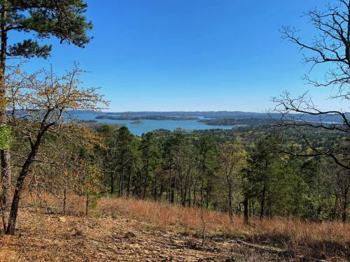 A scenic view of a lake surrounded by trees and hills under a clear blue sky.