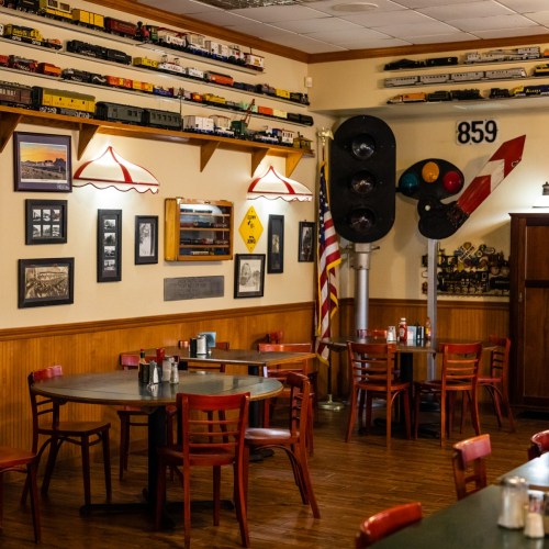 A cozy diner with model trains on the wall, red chairs, and a vintage traffic signal, featuring an American flag.