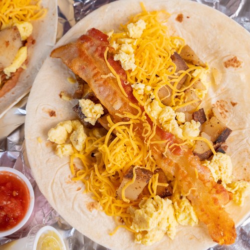 A close-up of a breakfast burrito filled with scrambled eggs, bacon, cheese, and potatoes, served with salsa.
