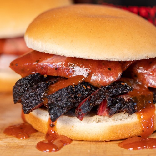 A close-up of a sandwich with layers of meat, sauce, and a soft bun, resting on a wooden surface.