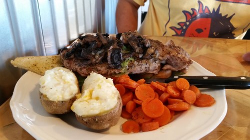 A plate featuring a grilled steak topped with mushrooms, baked potatoes, and steamed carrots.