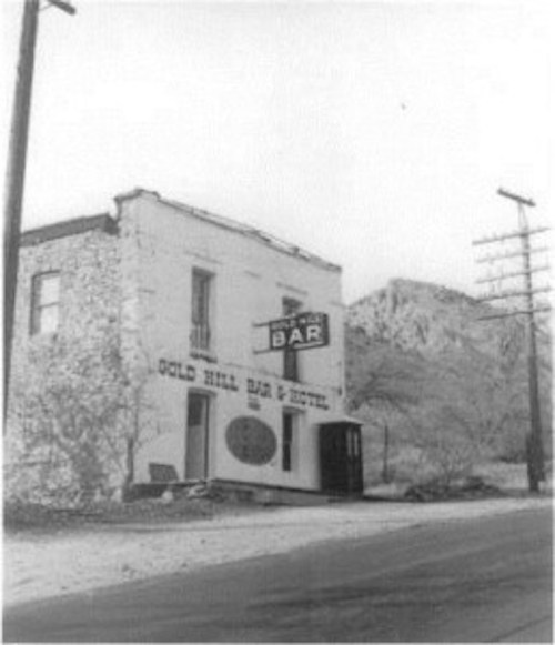 Black and white photo of the Gold Hill Bar & Hotel, a rustic building with a sign, surrounded by a barren landscape.
