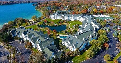 Aerial view of a resort by a lake, surrounded by colorful autumn trees and landscaped gardens.