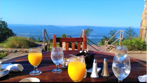 A table set with drinks, including orange juice and water, overlooking a scenic mountain view on a clear day.