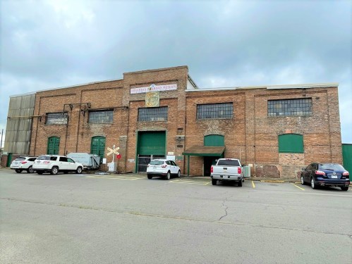 Exterior of a brick building with green doors, labeled as a museum, surrounded by parked cars and cloudy skies.