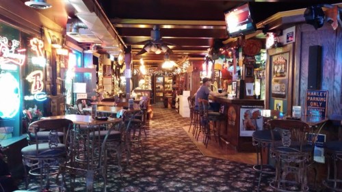 A cozy bar interior with wooden furniture, neon signs, and a long counter, creating a warm, inviting atmosphere.